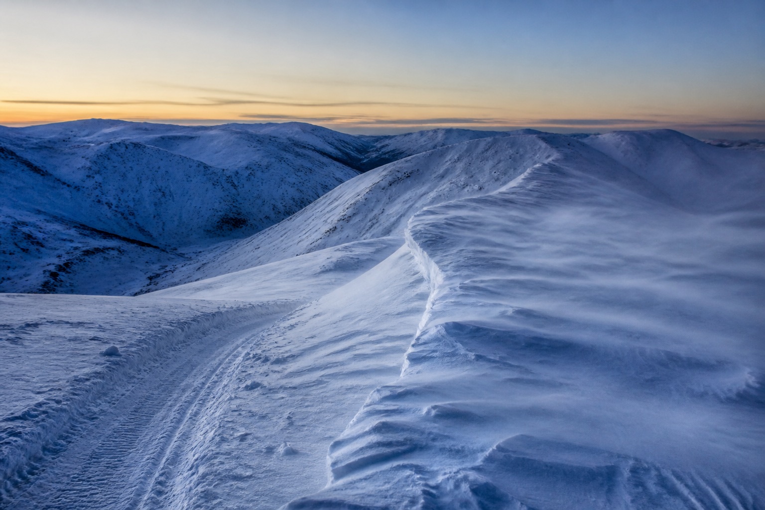 Wind-scoured unnamed mountain pass with a packed snowmobile line
